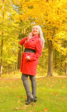 genç güzel artı kırmızı yün ceketli beyaz sarışın kadın sonbahar parkında yürüyor