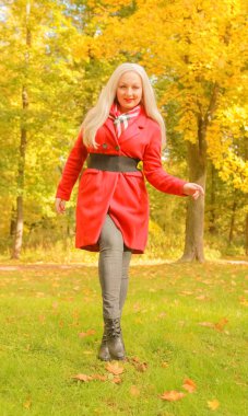 genç güzel artı kırmızı yün ceketli beyaz sarışın kadın sonbahar parkında yürüyor