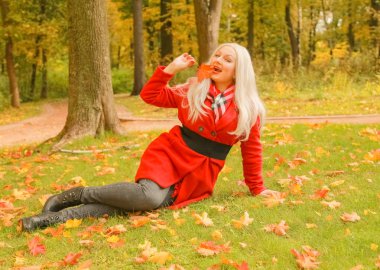 genç güzel artı kırmızı yün ceketli beyaz sarışın kadın sonbahar parkında yürüyor