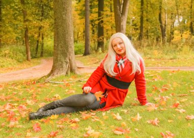 genç güzel artı kırmızı yün ceketli beyaz sarışın kadın sonbahar parkında yürüyor