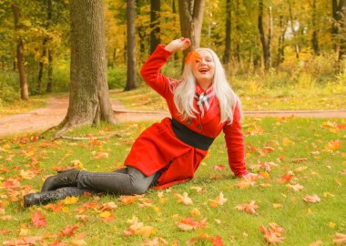 genç güzel artı kırmızı yün ceketli beyaz sarışın kadın sonbahar parkında yürüyor