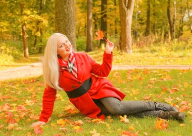 genç güzel artı kırmızı yün ceketli beyaz sarışın kadın sonbahar parkında yürüyor