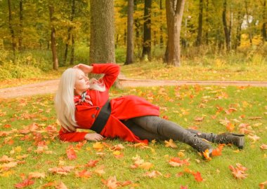 genç güzel artı kırmızı yün ceketli beyaz sarışın kadın sonbahar parkında yürüyor