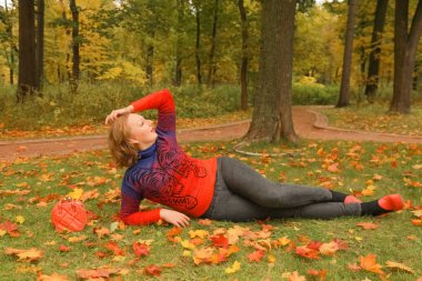 turuncu kazak genç güzel artı boyutu beyaz kadın sonbahar parkta yaprakları ile yere yatıyor