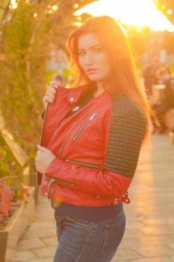 genç güzel artı kırmızı deri ceket li beyaz kadın gün batımı sonbahar parkında yürüyor