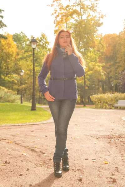 Kırmızı saçlı mor ceket giyen genç güzel beyaz kadın ve sonbahar parkı yürüyor — Stok fotoğraf
