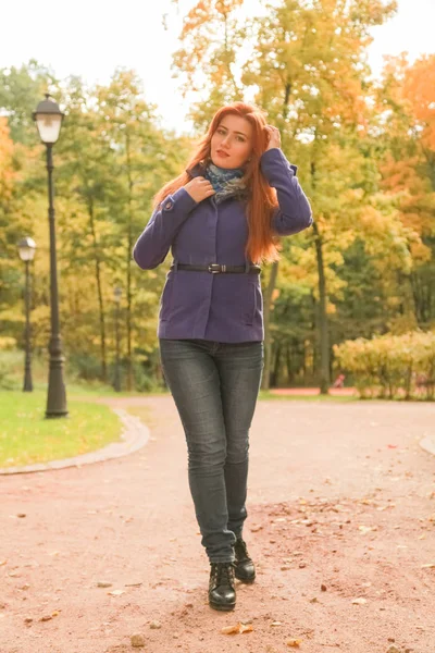 Jonge mooie Kaukasische vrouw met rood haar dragen paarse jas en wandelingen in herfst Park — Stockfoto