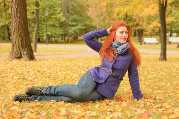 Молодая красивая белая женщина с рыжими волосами в фиолетовой куртке и прогулки в осеннем парке — стоковое фото