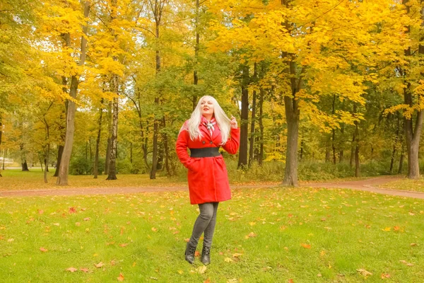 genç güzel artı kırmızı yün ceketli beyaz sarışın kadın sonbahar parkında yürüyor