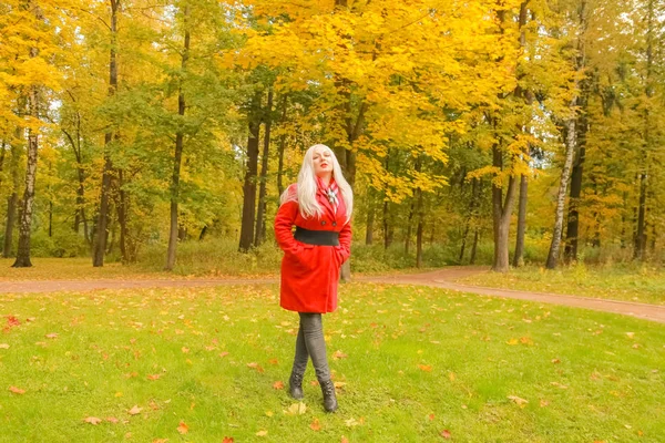 genç güzel artı kırmızı yün ceketli beyaz sarışın kadın sonbahar parkında yürüyor