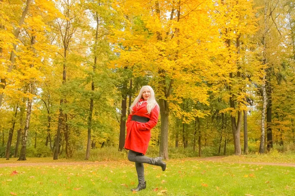 genç güzel artı kırmızı yün ceketli beyaz sarışın kadın sonbahar parkında yürüyor