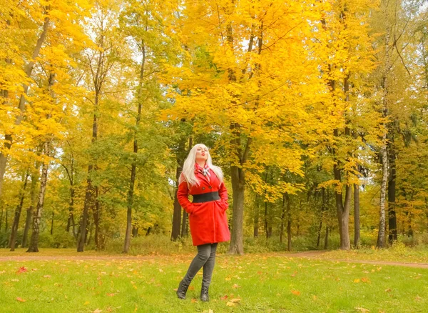 Jonge mooie plus size Kaukasische blonde vrouw in rode wol vacht wandelingen in herfst Park — Stockfoto