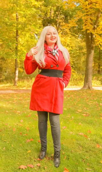 genç güzel artı kırmızı yün ceketli beyaz sarışın kadın sonbahar parkında yürüyor