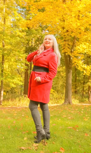 genç güzel artı kırmızı yün ceketli beyaz sarışın kadın sonbahar parkında yürüyor