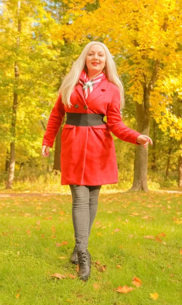 genç güzel artı kırmızı yün ceketli beyaz sarışın kadın sonbahar parkında yürüyor