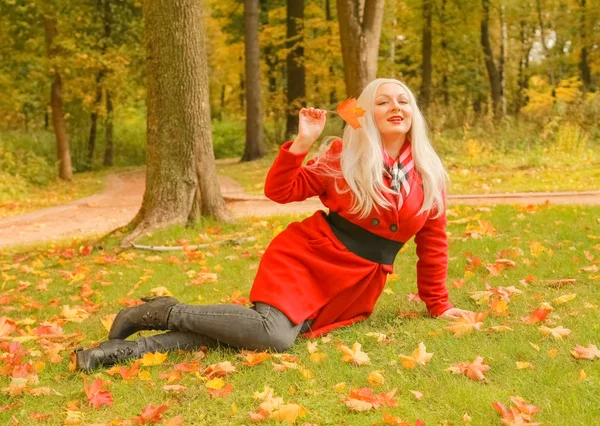 genç güzel artı kırmızı yün ceketli beyaz sarışın kadın sonbahar parkında yürüyor