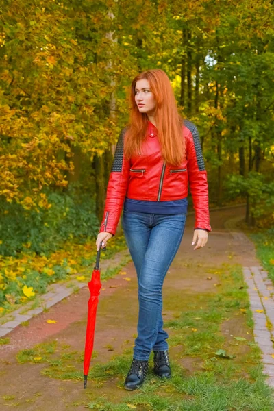 Молодая красивая белая женщина с красным зонтиком гуляет в осеннем парке — стоковое фото