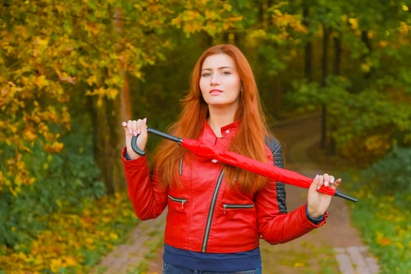 Jovem bonita plus tamanho mulher caucasiana caminha com guarda-chuva vermelho no parque de outono — Fotografia de Stock