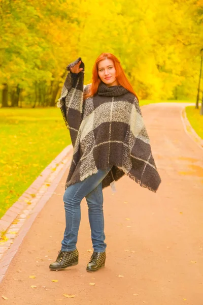 Jonge mooie plus size Kaukasische vrouw in geruite wollen poncho wandelingen in herfst Park — Stockfoto