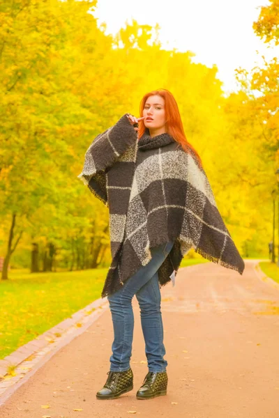 Junge hübsche Plus-Size-Kaukasierin im karierten Wollponcho spaziert im Herbst-Park — Stockfoto