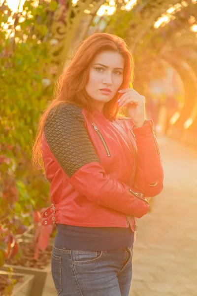 Młody ładny plus rozmiar kaukaski kobieta w czerwonym skórzanym płaszczu spacery w Sunset Autumn Park — Zdjęcie stockowe