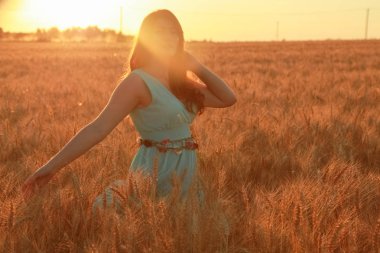 gün batımında altın olgun buğday alanında yürüyen elbiseli kız