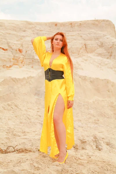 Vrouw in gele lange jurk met rood haar staande in het witte zand — Stockfoto