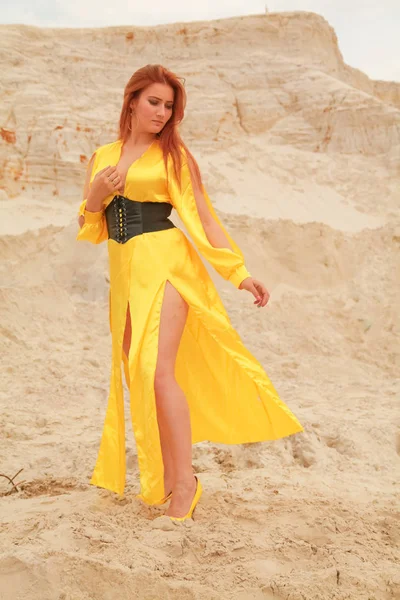 Femme en robe longue jaune avec les cheveux roux debout dans le sable blanc — Photo