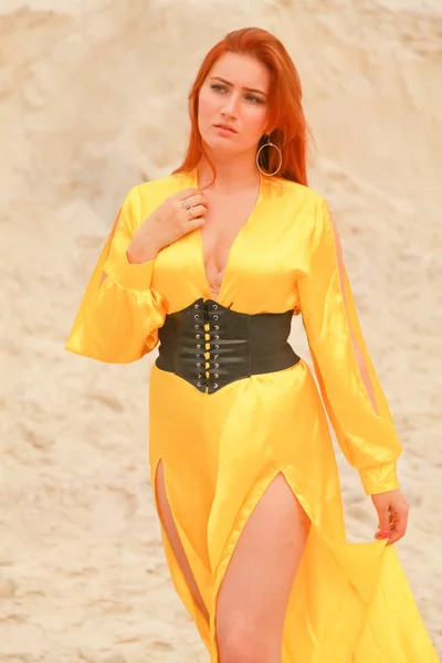 Mujer en vestido largo amarillo con el pelo rojo de pie en la arena blanca —  Fotos de Stock
