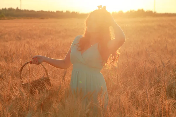 Meisje in jurk wandelen in gouden rijpe tarwe veld bij zonsondergang — Stockfoto