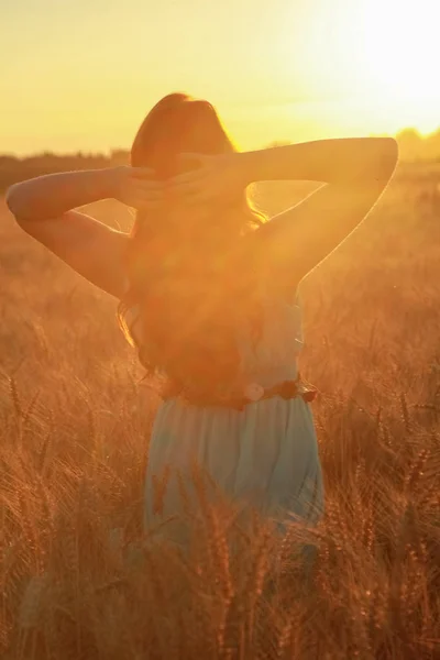 Meisje in jurk wandelen in gouden rijpe tarwe veld bij zonsondergang — Stockfoto