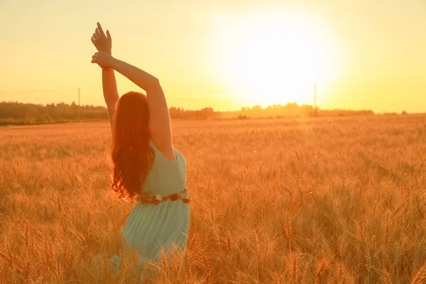 girl in dress walking in golden ripe wheat field at sunset