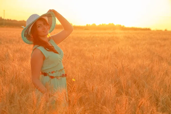 Niña en vestido caminando en el campo de trigo maduro dorado al atardecer —  Fotos de Stock