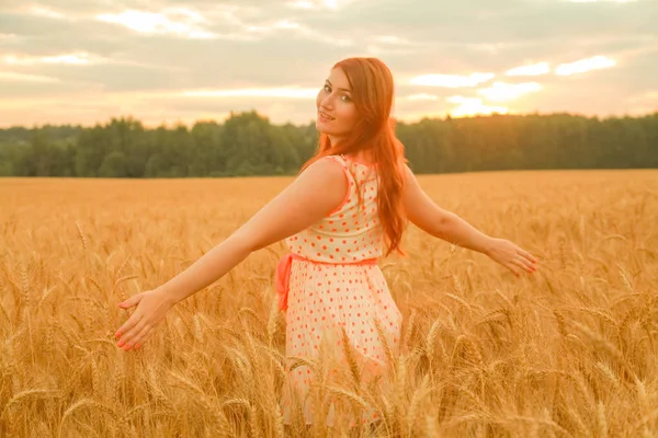 Menina de vestido andando no campo de trigo maduro dourado ao pôr do sol — Fotografia de Stock