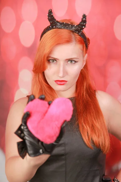 Chica diabólica con peluche rosa con forma de corazón sobre fondo rojo — Foto de Stock