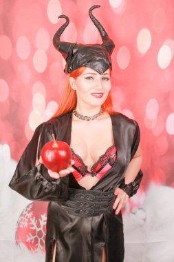 şeytan boynuzları ile seksi siyah elbise kızıl saçlı kız ayartma ve baştan çıkarma ile kırmızı elma tutar
