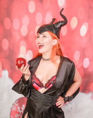 şeytan boynuzları ile seksi siyah elbise kızıl saçlı kız ayartma ve baştan çıkarma ile kırmızı elma tutar