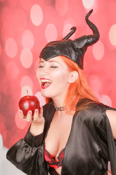 Redheaded dziewczyna w seksownej czarnej sukni z rogami diabła trzyma Czerwone jabłko z pokusą i uwodzenia — Zdjęcie stockowe