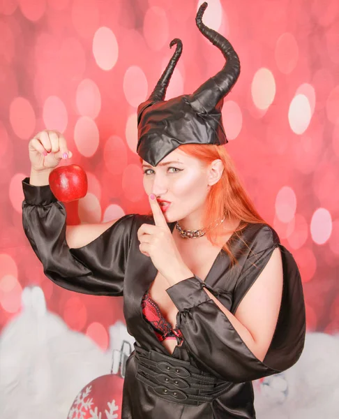 Menina ruiva em vestido preto sexy com chifres do diabo detém maçã vermelha com tentação e sedução — Fotografia de Stock