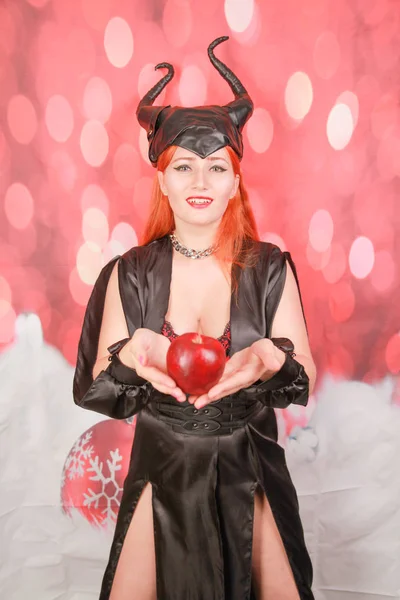 şeytan boynuzları ile seksi siyah elbise kızıl saçlı kız ayartma ve baştan çıkarma ile kırmızı elma tutar