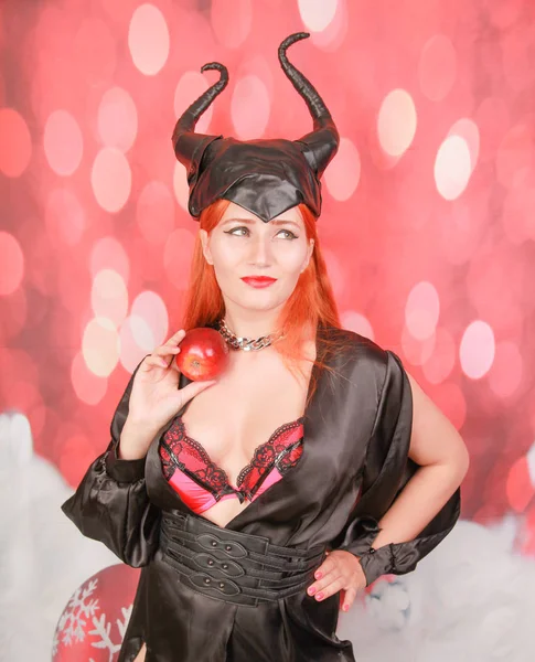 şeytan boynuzları ile seksi siyah elbise kızıl saçlı kız ayartma ve baştan çıkarma ile kırmızı elma tutar