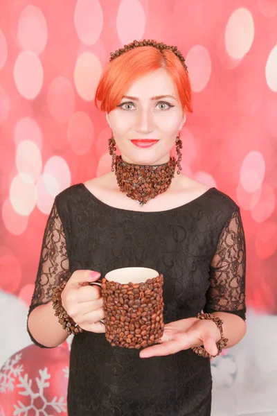 女人享受咖啡杯的美味香气，在红色圣诞背景下佩戴带咖啡豆的珠宝 — 图库照片
