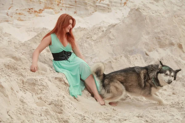 Concepção engraçada dos melhores amigos. Jovem feliz pessoa feminina caminha no deserto com cão grande malamute ao ar livre — Fotografia de Stock