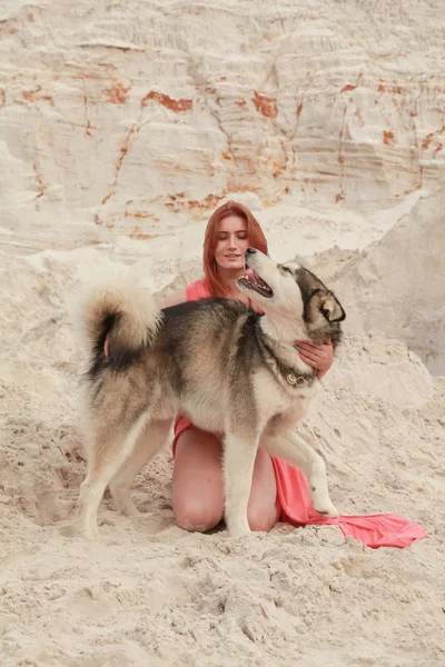 Concepção engraçada dos melhores amigos. Jovem feliz pessoa feminina caminha no deserto com cão grande malamute ao ar livre — Fotografia de Stock