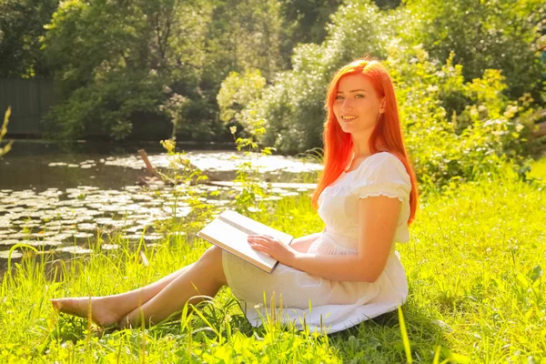 Tiener meisje met rood haar in witte katoenen jurk rusten en lezen van het boek in een zomer Hot City Park — Stockfoto