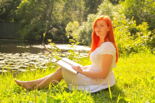 Tiener meisje met rood haar in witte katoenen jurk rusten en lezen van het boek in een zomer Hot City Park — Stockfoto
