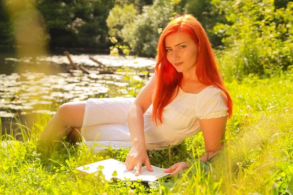 Teenager-Mädchen mit roten Haaren im weißen Baumwollkleid ruhen und lesen das Buch in einem sommerlich heißen Stadtpark — Stockfoto