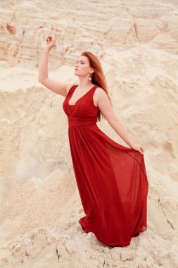 Genç güzel artı boyutu kırmızı uzun elbiseli beyaz kadın kum ile çöl manzara poz.