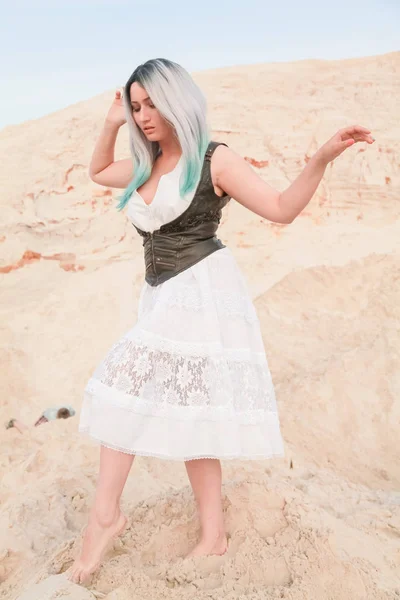 Jovem mulher branca bonita em vestido branco e colete de couro marrom posando na paisagem do deserto com areia . — Fotografia de Stock