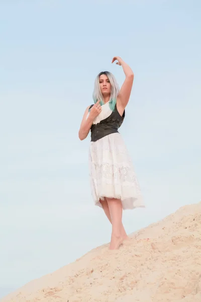 Jeune belle femme caucasienne en robe blanche et gilet en cuir marron posant dans un paysage désertique avec du sable . — Photo